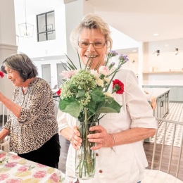a woman smiling while she holds a vase of flowers